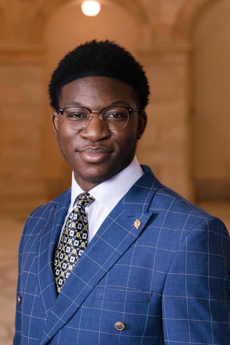 Ademola in a blue suit and tie, with a Maryland flag pin